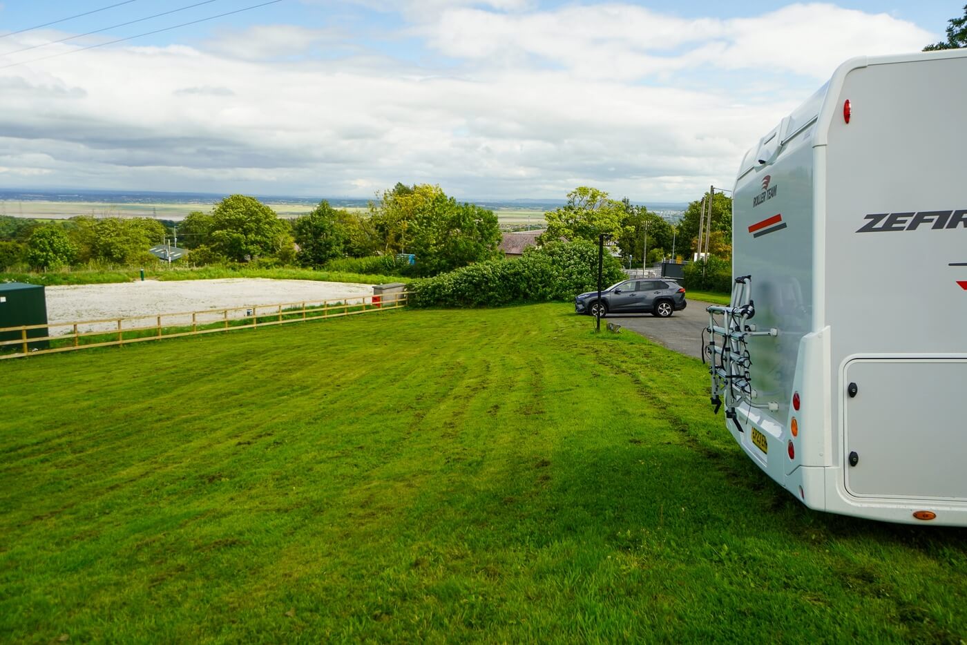 Wohnmobil neben einer Rasenfläche in ländlicher Umgebung.
